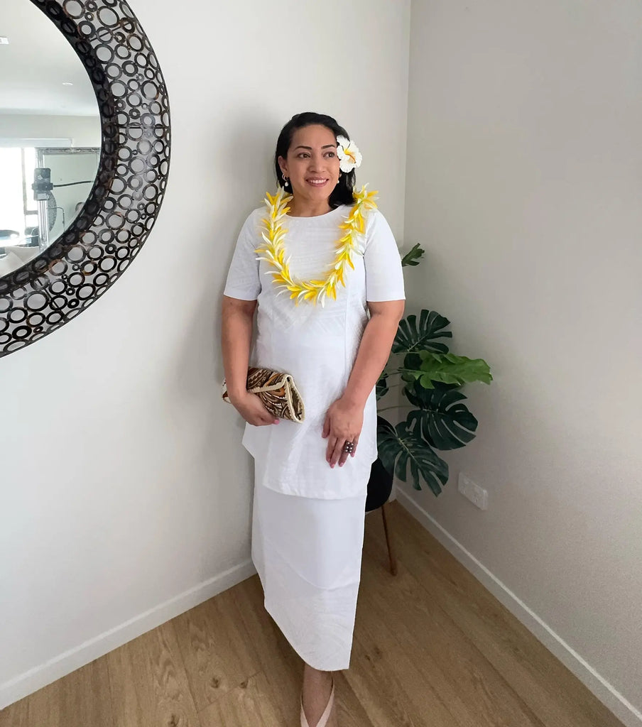 Model wearing an elegant white puletasi with traditional Pacific-inspired design, standing gracefully to showcase the modest fit and cultural beauty of the outfit—perfect for formal occasions or cultural celebrations.